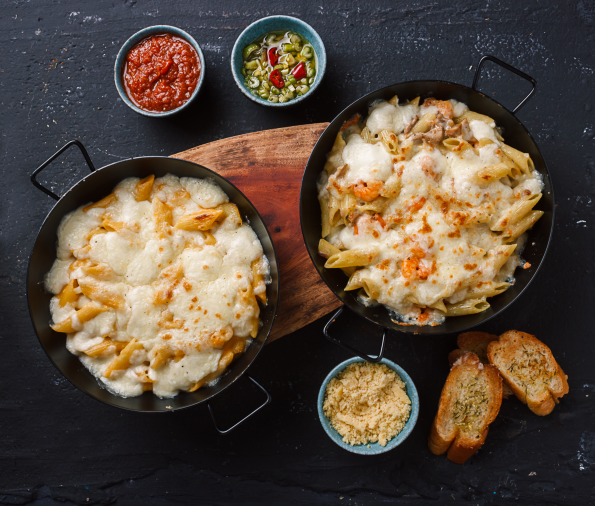 Delicious macaroni with cheese served on table with toasted bread and sauce bowls