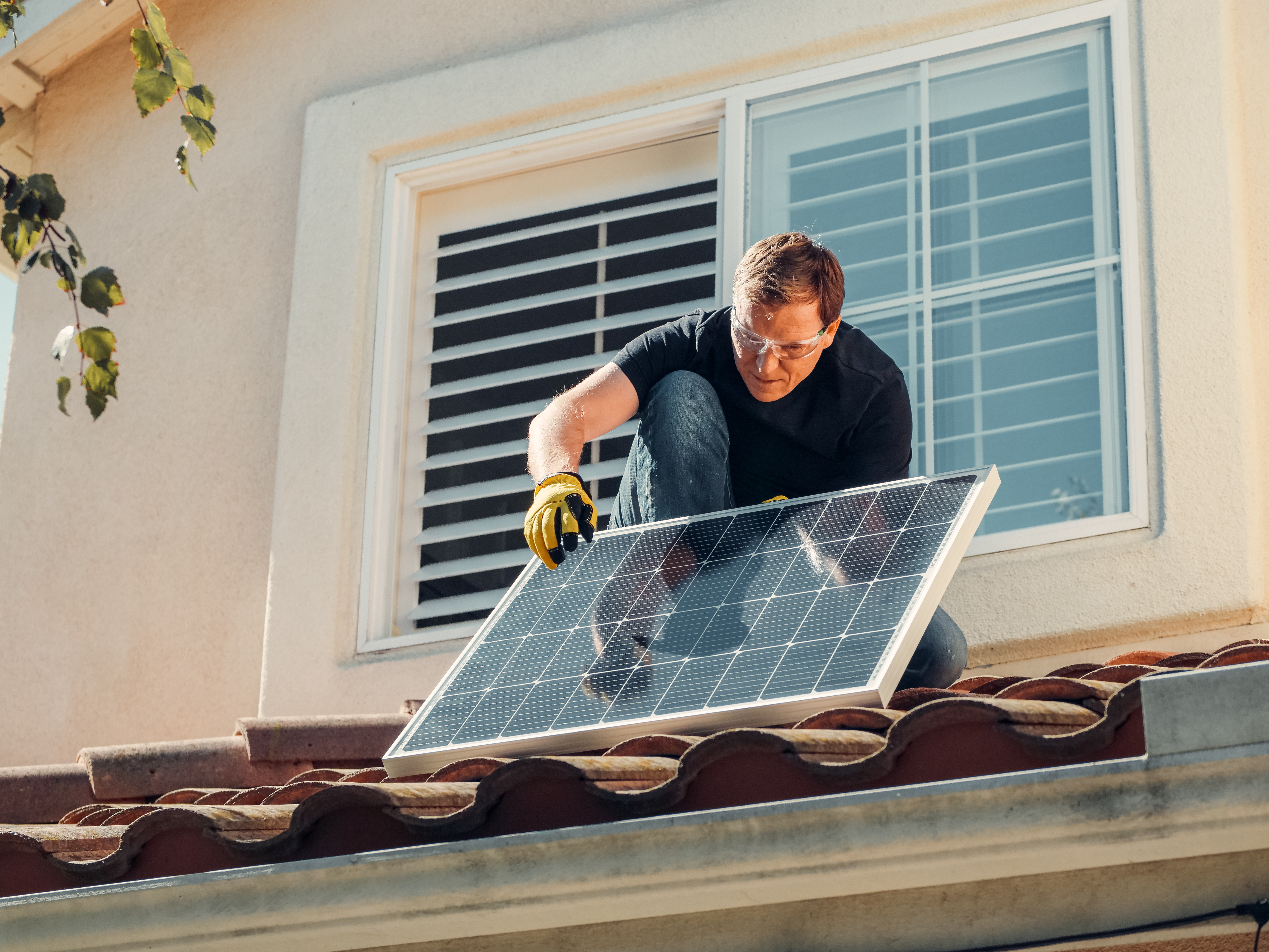 Man with gloves holding solar panels on the roof